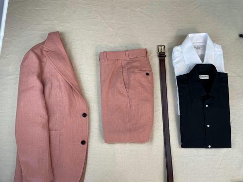 Salmon suit laid out with brown leather belt and a black collared shirt and a white collared shirt